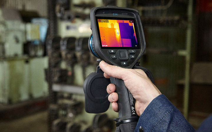 A hand holding a device showing a thermography heat map of electrical equipment