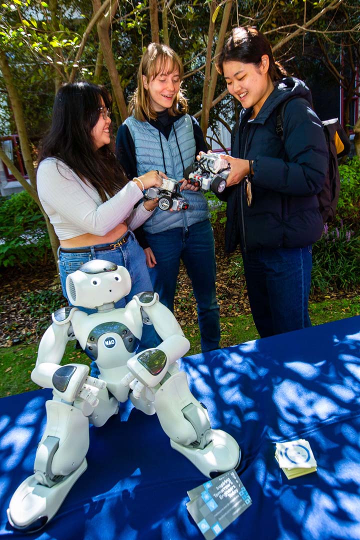 Robot figurine in the foreground is facing the camera while a group of students talk in the background