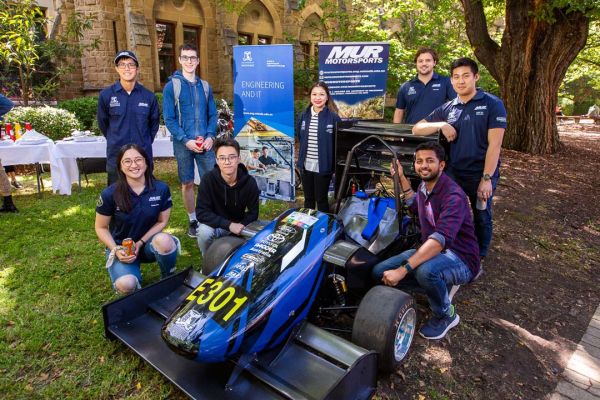 Melbourne Uni Rover Team crowd around the racecar smiling at the camera