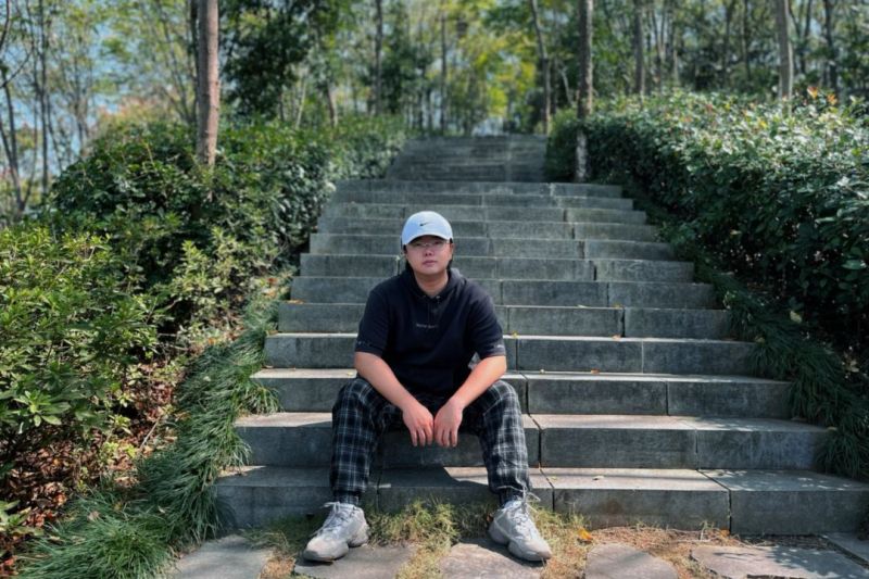 Person seated in front of outdoor stairway surrounded by trees.
