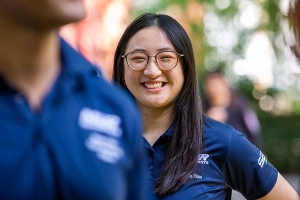Female student smiles at the camera from behind another student in a blue Melbourne Uni Rover team shirt