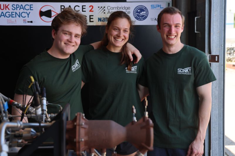 Three people standing behind rocket engine.