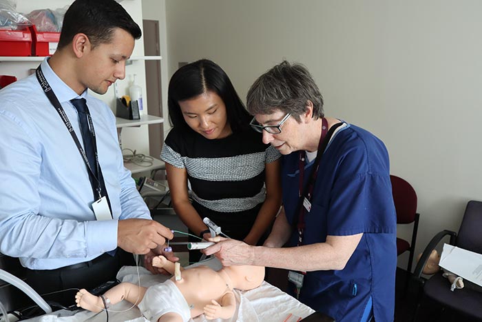 Edward, Amy and a healthcare worker using their device on a model of a baby