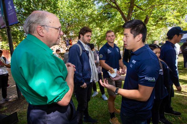 Students from the Rover club stand talking with academic staff on the South Lawn of the Parkville campus.