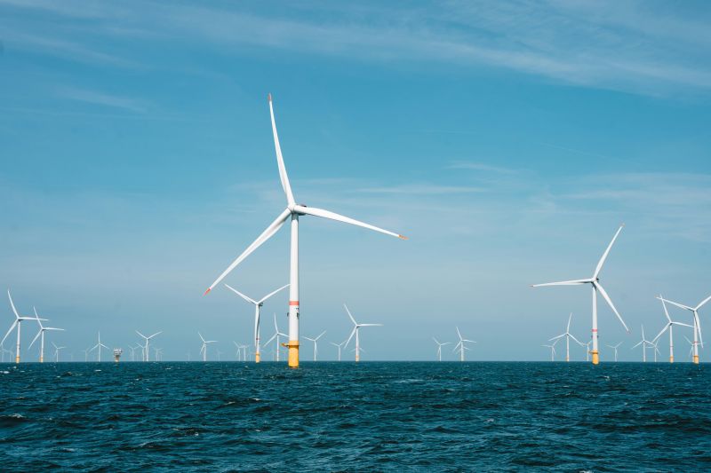A range of offshore wind turbines in the ocean with a blue sky in the backgroun.
