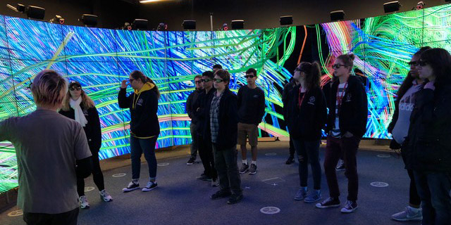 A group of students stand in front of a series of projection screens.