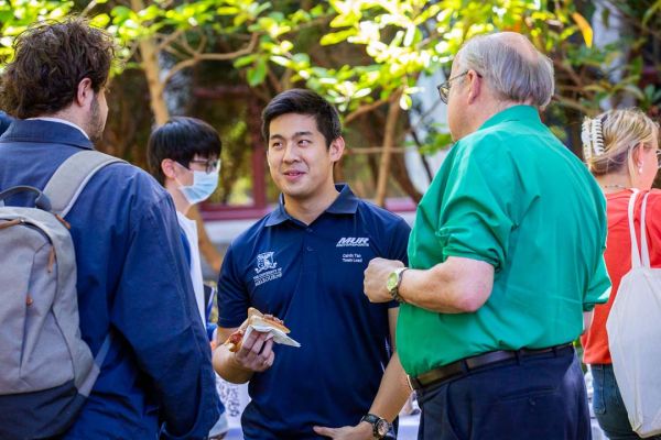 Two students in navy blue shirts talk with an academic staff member in a bright green shirt.