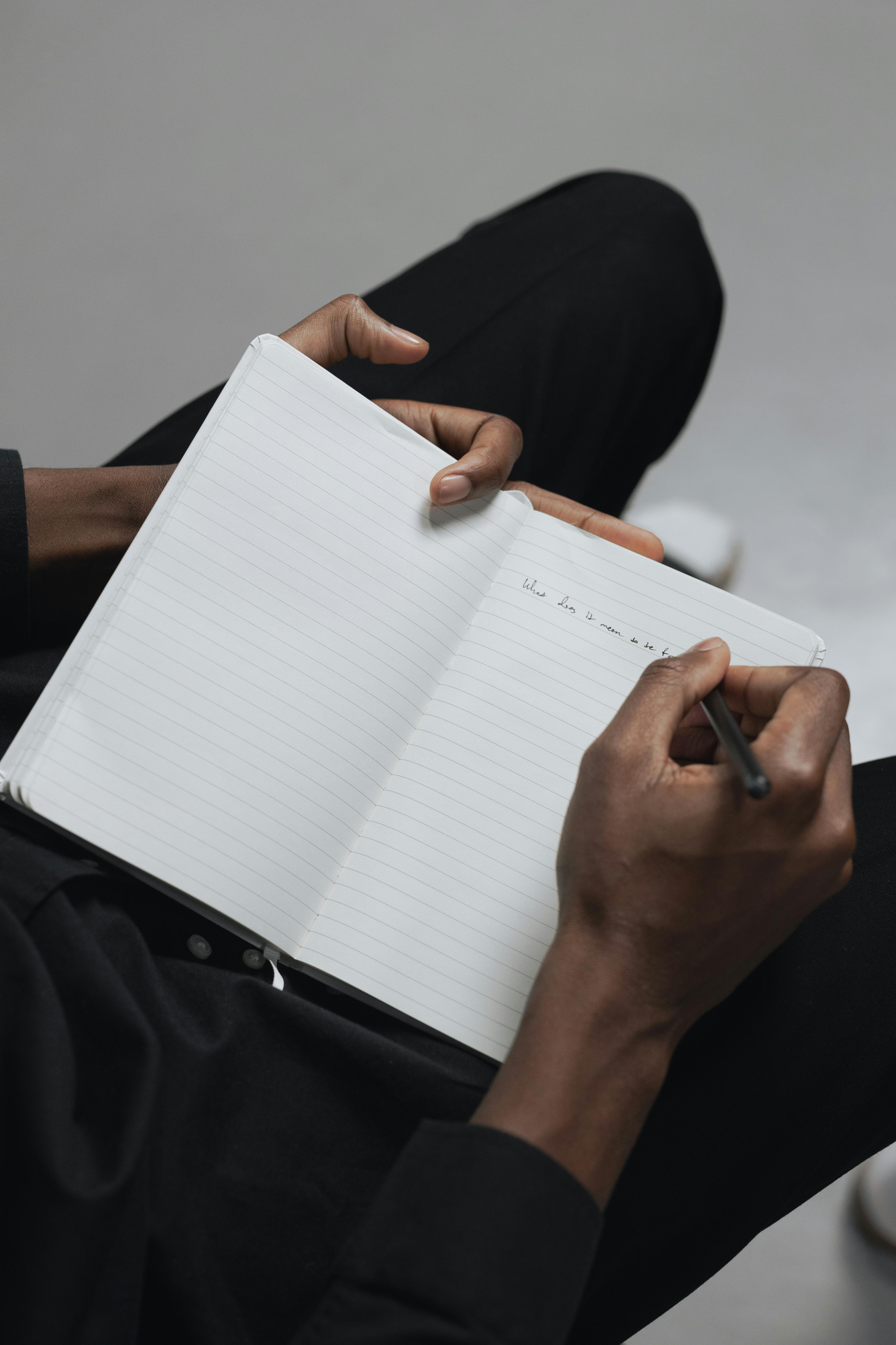 Close up of book with a person writing in it on their lap 