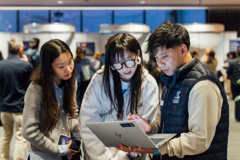 Three people crowd around a bright ipad