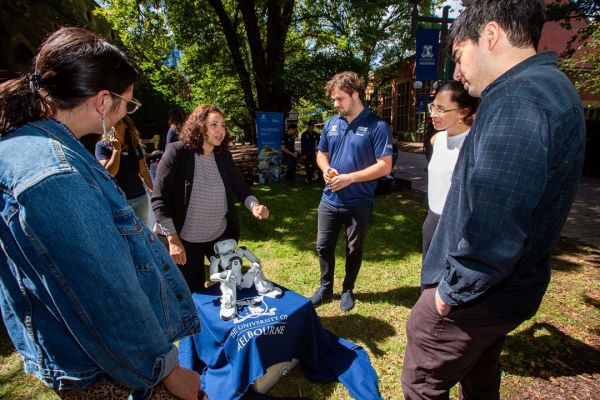 Students and academics group around a low table with a white robot figurine positioned on a blue tablecloth.