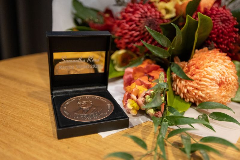 Close up image of bronze medal, next to a flower bouquet