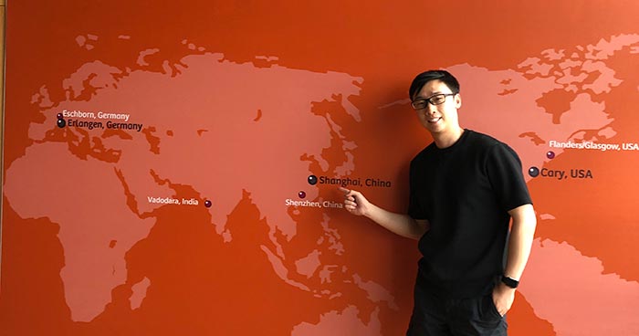 Yicheng Zhang in front of wall with world map depicted on it