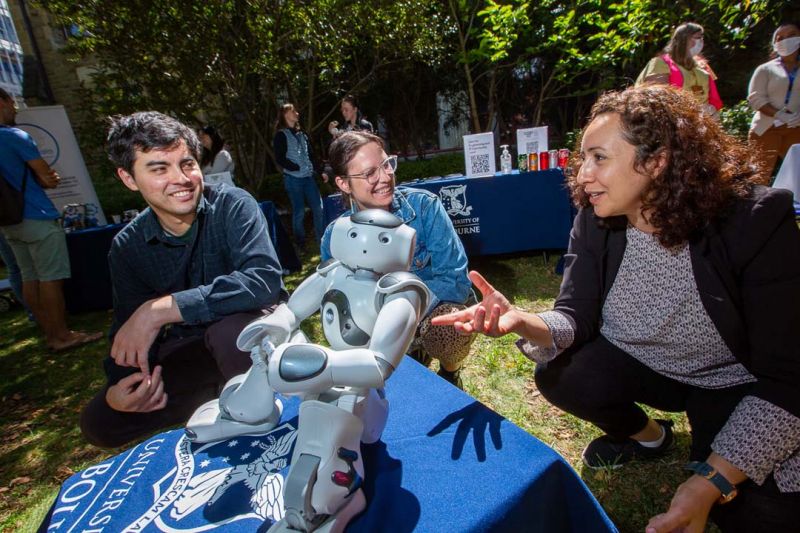 Students and staff talk while gesticulating to a white robot figurine