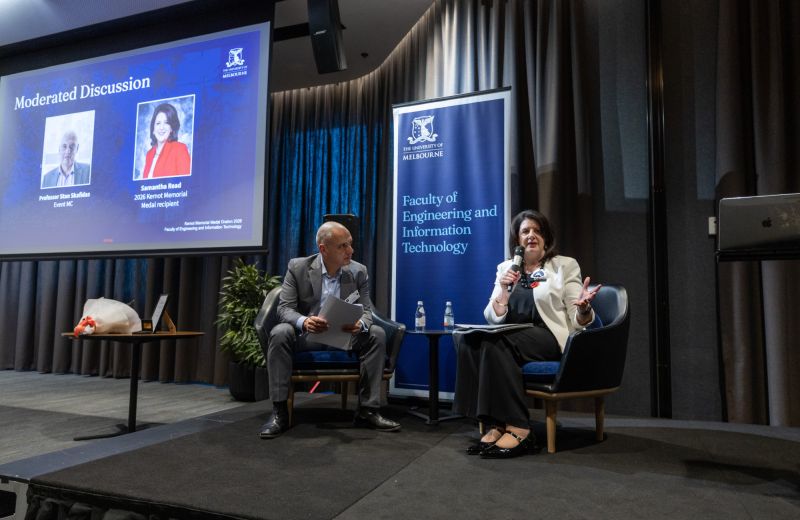 Two people seatoned, one speaking into mic