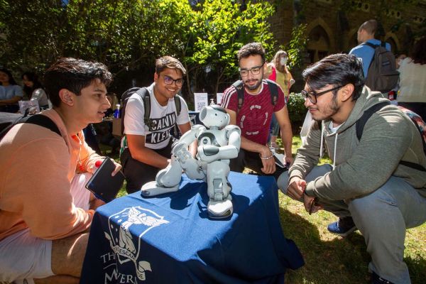 Four male students kneel by a low table looking at a white robot figurine