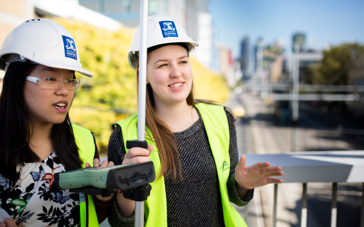 Two female students in hard hats with survey equipment
